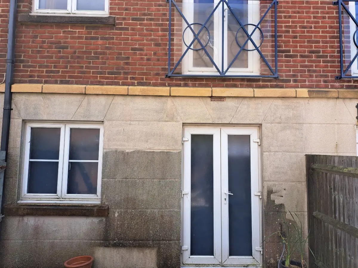 Rendered and stone wall with damp staining around a window, door and downpipe
