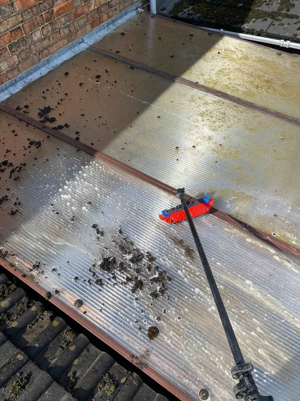 Conservatory roof panel being cleaned with a telescopic brush, with algae, dirt and debris on the glazing